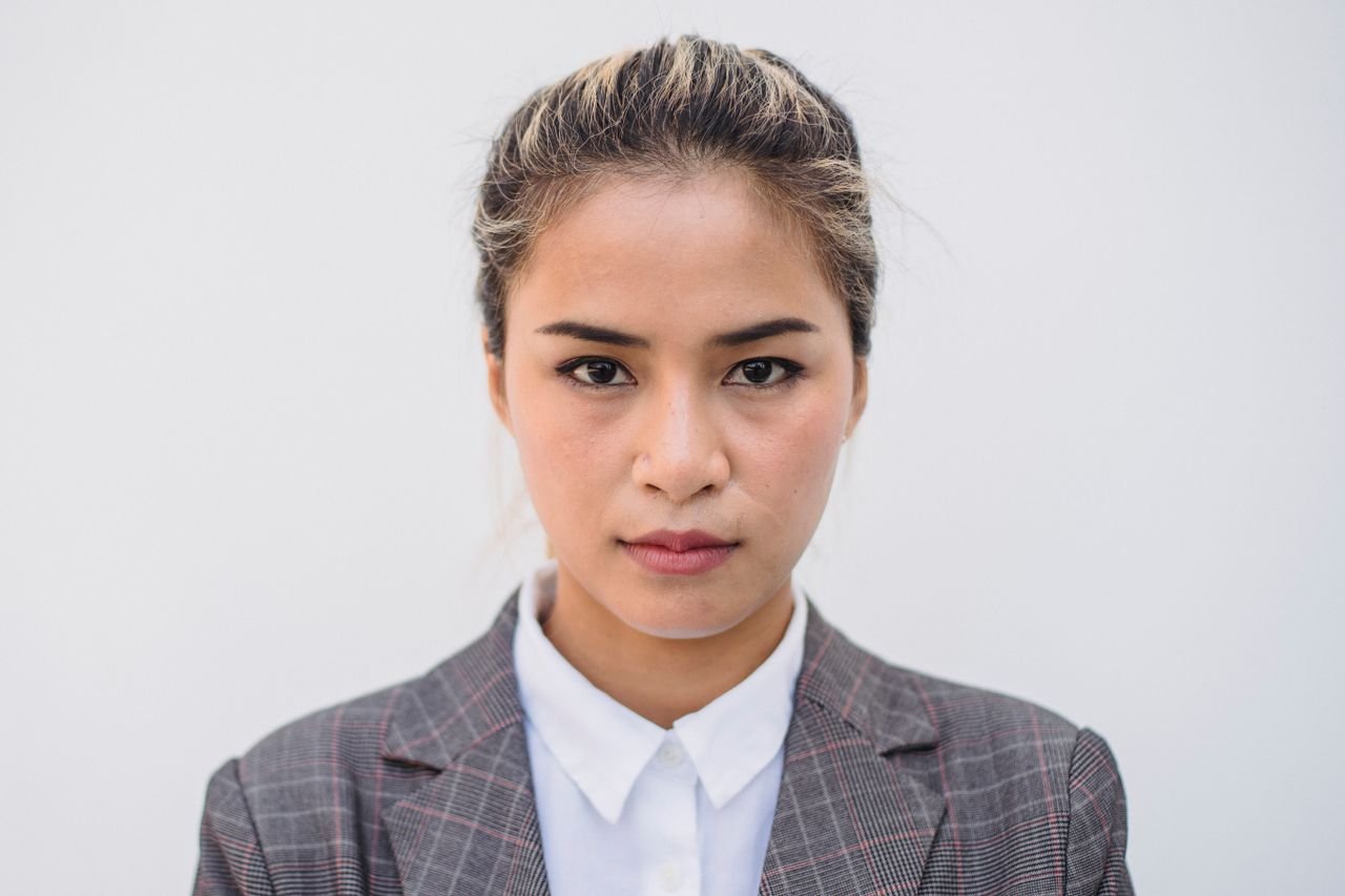 Portrait of a confident Asian woman wearing a plaid blazer and white shirt against a plain background.